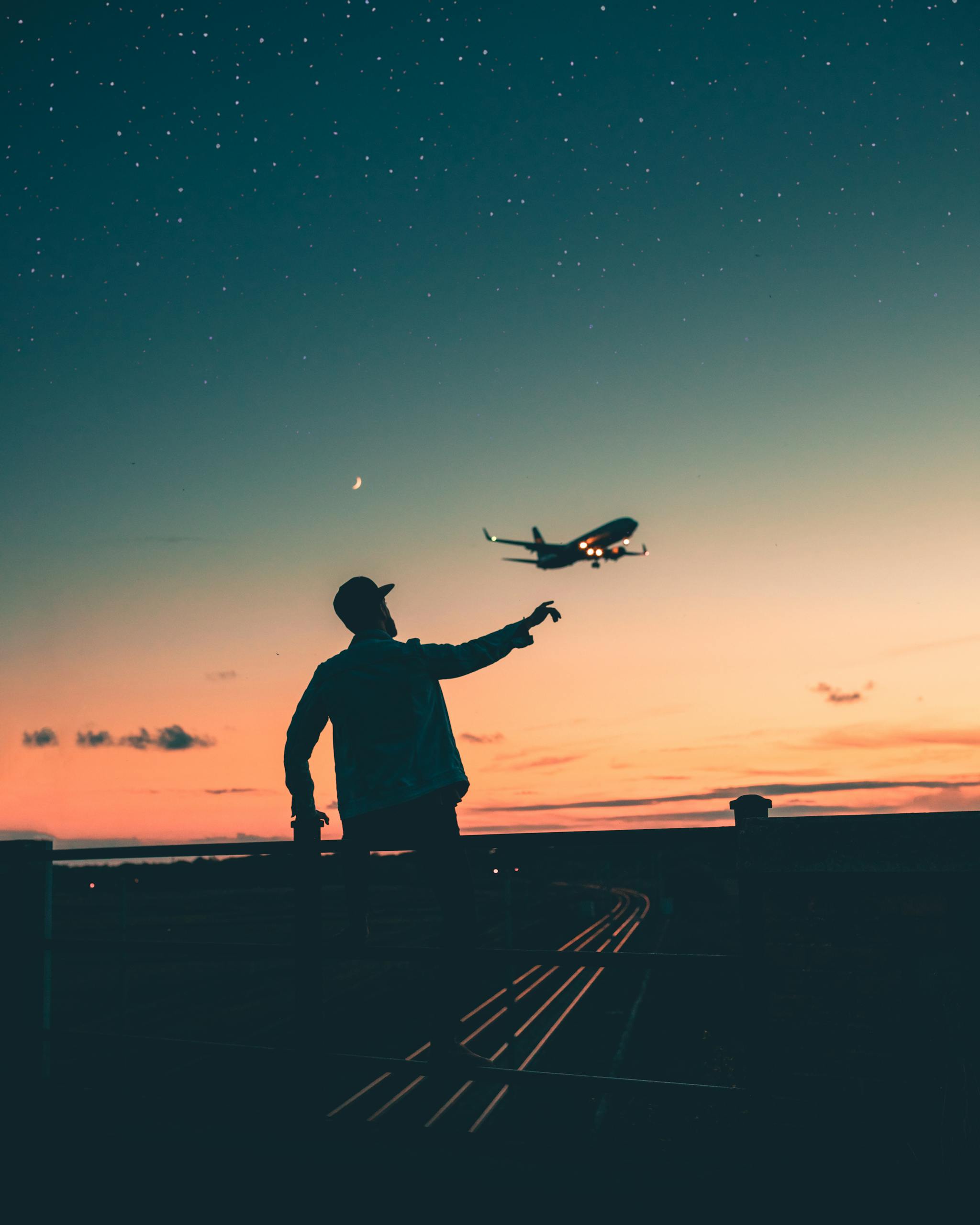 A silhouette of a person pointing at a flying airplane under a starry twilight sky.